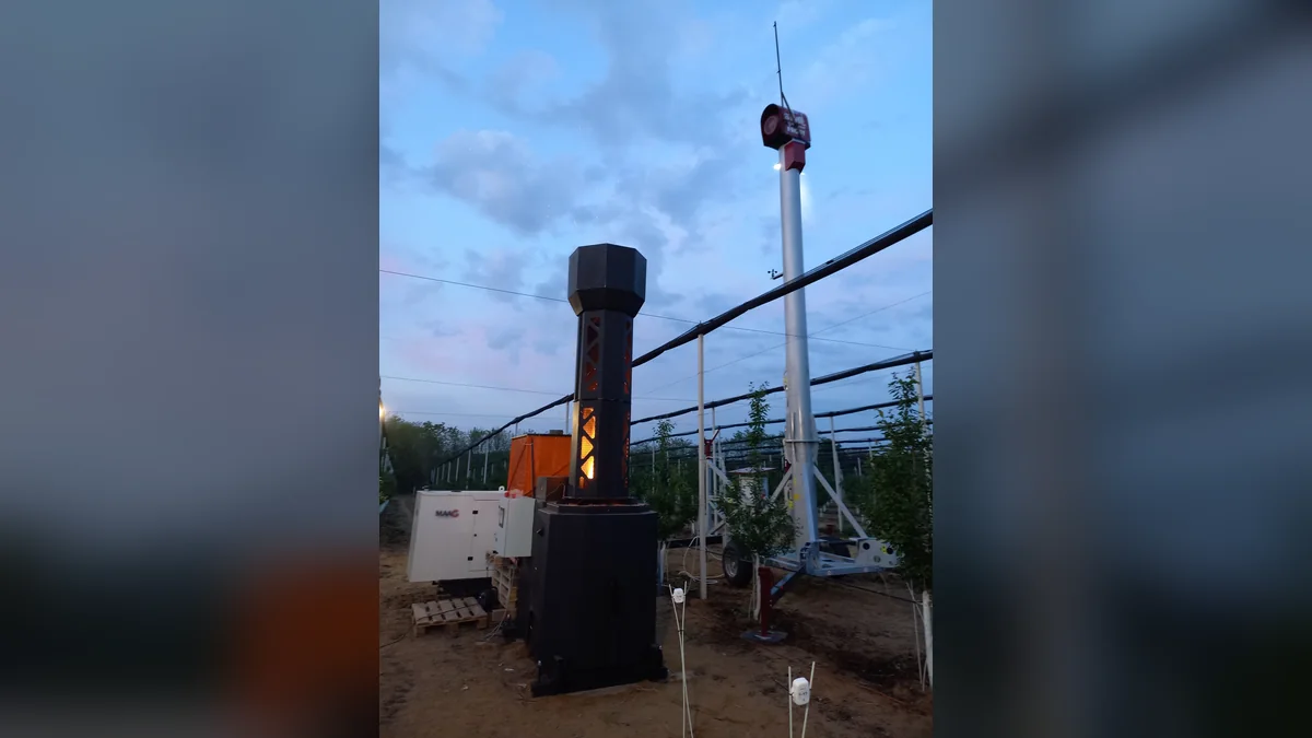 Vormair hőgenerátor lángoló kéménnyel egy ültetvényben, mellette szélgép